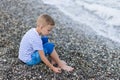 Boy in a striped t-shirt sitting close by the water at the beach