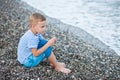 Boy in a striped t-shirt sitting close by the water at the beach