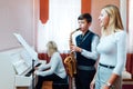 Boy student learns to play the saxophone in a music lesson to accompaniment of the piano