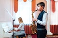 Boy student learns to play the saxophone in a music lesson to accompaniment of the piano