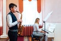 Boy student learns to play the saxophone in a music lesson to accompaniment of the piano