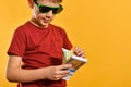 A boy in sunglasses considers banknotes in a bundle, a glamorous and stylish child with currency on a yellow background