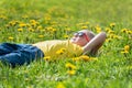 Boy in sunglasses lying down in the green grass. Child rest in dandelions flower filed. Sunny day Royalty Free Stock Photo