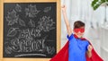 boy in super hero costume over school blackboard