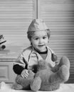 Boy in surgical uniform and stethoscope on neck on wooden background. Kid in doctor coat plays with teddy bear Royalty Free Stock Photo