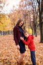 Boy is surprised to listen to the belly of his pregnant mother. Autumn park on the background