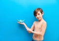 A boy in swimming trunks holds a paper boat on a blue background. Background travelers, sea adventures. Fun at the water park and Royalty Free Stock Photo