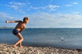 Boy in swimming trunks on lake throws stones into water. Teenager plays on seashore. Summer vacation with parents on lake on