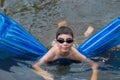 Boy swims on blue mattress in the river
