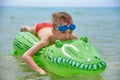 BOY SWIMS IN THE SEA ON THE INFLATABLE CROCODYLE TOY