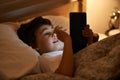 Boy, tablet and bed with night, digital and technology for social media or learning. Child, bedroom and connectivity for Royalty Free Stock Photo