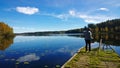 The boy takes a picture of a beautiful lake in autumn day. The view from the back