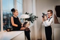 A boy takes a picture of a girl sitting on the window sill with a book in her hands Royalty Free Stock Photo