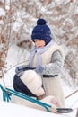 The boy is taking his teddy bear on a sledge to visit Santa Claus.