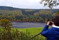 Boy taking photograph of view of river with autumn foliage