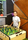 Boy teenager in a blue shirt plays in a table football with figures of football players of both teams in a wooden box in the Royalty Free Stock Photo