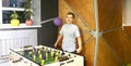 Boy teenager in a blue shirt plays in a table football with figures of football players of both teams in a wooden box in the Royalty Free Stock Photo