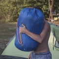 Boy teenager carrying bag with tent in summer campsite.