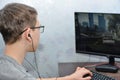 Boy teenager in glasses and headphones plays computer games and looks at the monitor