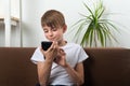 Boy teenager holds smartphone in his hands and smiles. Child at home on couch with phone in his hands