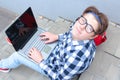 Boy teenager schoolboy or student is sitting on the stairs, working in the computer, wearing glasses, in a shirt, smiling, red b Royalty Free Stock Photo