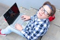 Boy teenager schoolboy or student is sitting on the stairs, working in the computer, wearing glasses, in a shirt, smiling, red b Royalty Free Stock Photo