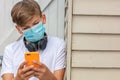 Boy teenager teen male child wearing face mask Using Phone and Headphones in Coronavirus COVID-19 Pandemic Royalty Free Stock Photo