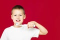 Boy teenager 7-10 in a white t-shirt with electric toothbrush and toothpaste brushes his teeth on a red background