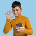 Boy teenager in a yellow sweater, with a smartphone in hand, onine communication, welcomes the interlocutor, smiling