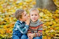 A boy tells a secret to his friend in the ear in an autumn Park against a background of yellow leaves. The boys smile