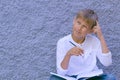 Boy thinking with a finger on the forehead. Kid sitting on the ground and doing school homework. Royalty Free Stock Photo