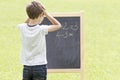 Boy thinking, writing and counting on blackboard. Green outdoor background Royalty Free Stock Photo