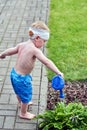 Boy three years watering flowers from a watering can. On head bandage with blood Royalty Free Stock Photo