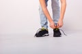 Boy ties shoelaces on sneakers, only hands and feet on white background