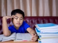 A boy is tired of reading a book on a wooden table. with a pile of books beside The background is a red sofa and cream curtains Royalty Free Stock Photo