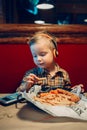 boy toddler playing digital toy cell phone gadget with ear phones and eating food meal in restaurant Royalty Free Stock Photo