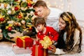 A boy together with his parents unpacks a gift box on Christmas Eve near a festively decorated Christmas tree Royalty Free Stock Photo