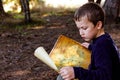 Boy trying to read an old travel map, lost in a forest, in search of adventure Royalty Free Stock Photo