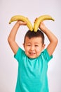 Child boy in turquoise shirt, holding bananas depicting horns and smiling - fruits and healthy food Royalty Free Stock Photo