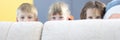 Boy and two girls hide behind sofa and look out. Royalty Free Stock Photo