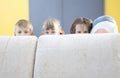 Boy and two girls hide behind sofa and look out. Royalty Free Stock Photo