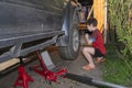 Boy unscrews the nuts on the wheel of big off-road car. Wheel replacement in the yard Royalty Free Stock Photo