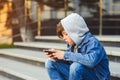 Boy use phone and plays games. Kid in the hood sitting on the stairs. Kids addicted online games and cartoons. Schoolboy plays on Royalty Free Stock Photo