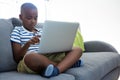 Boy using laptop while sitting with crossed legged on sofa at home Royalty Free Stock Photo