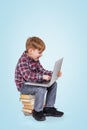 Boy using laptop while sitting on stack of books Royalty Free Stock Photo