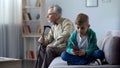 Boy using mobile phone, upset granddad sitting aside, internet addiction concept Royalty Free Stock Photo