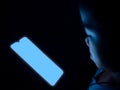 A boy is using a phone with a blank blue screen on a dark black background Royalty Free Stock Photo