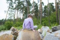 the child sits on the bark of large stones in front of a pine forest. Royalty Free Stock Photo