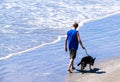 Teenage boy walks his dog on a beach near the edge of the ocean