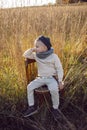 boy in warm clothes sit on chair along a path on a field with dried grass